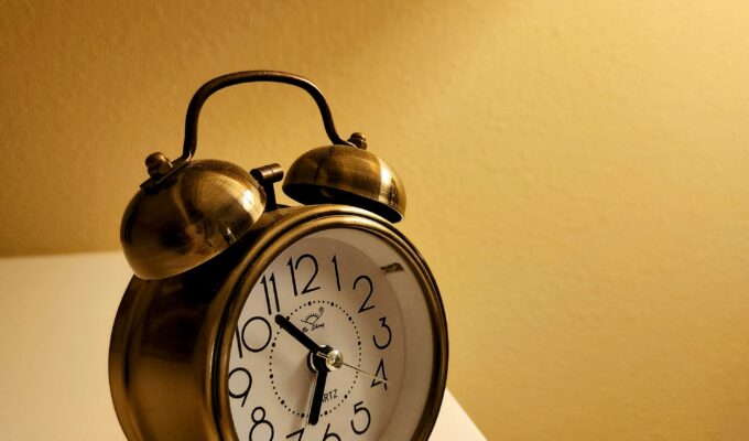 A gold alarm clock sitting on a white surface against a yellow background