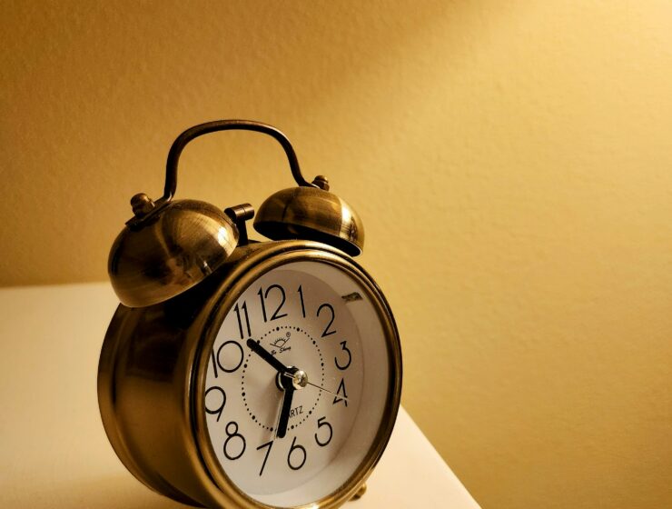 A gold alarm clock sitting on a white surface against a yellow background