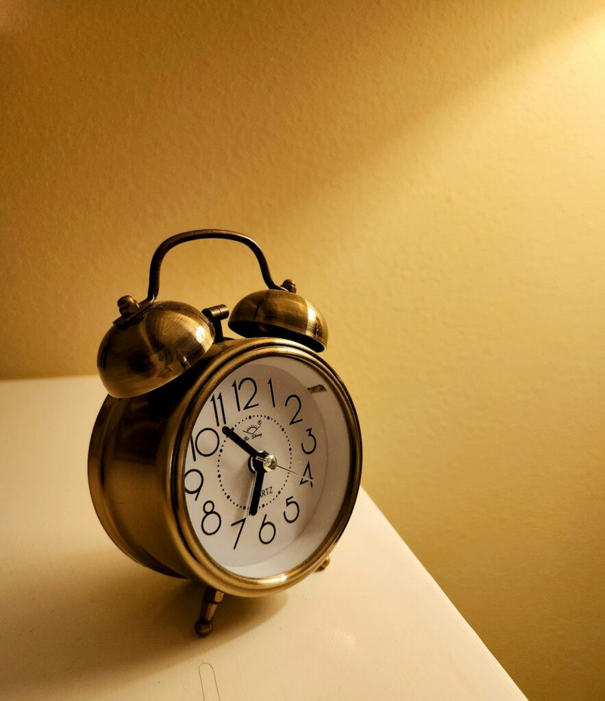 A gold alarm clock sitting on a white surface against a yellow background